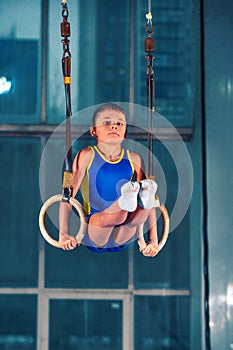 Full length rearview shot of a male athlete performing pull-ups on gymnastic rings.