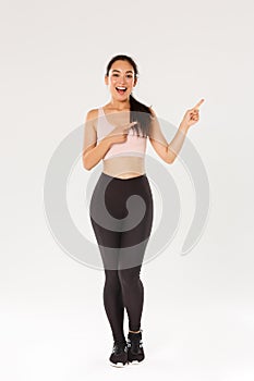 Full length of sassy attractive female athelte, asian fitness girl in sportswear pointing fingers upper right corner