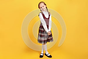 Full-length schoolgirl in uniform on a yellow background. Cute little girl is smiling and looking at the camera