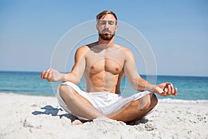 Full length of shirtless man meditating at beach