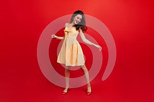 Full-length shot of active woman dancing on red background. Lady in sundress and heels having fun.