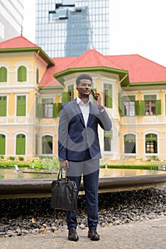 Full length shot of African businessman outdoors talking on mobile phone