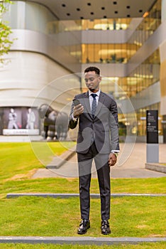 Full length shot of African businessman standing outdoors and using phone