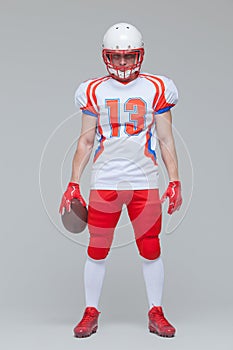 Full length shot of american football sportsman player wearing helmet holding rugby ball isolated on grey background