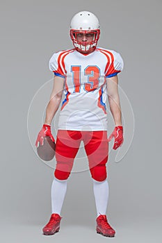 Full length shot of american football sportsman player wearing helmet holding rugby ball isolated on grey background