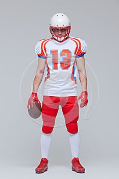 Full length shot of american football sportsman player wearing helmet holding rugby ball isolated on grey background