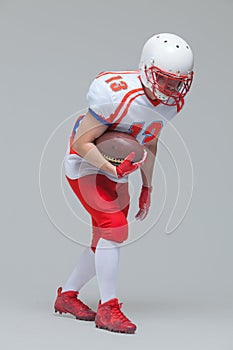 Full length shot of american football sportsman player wearing helmet posing with rugby ball isolated on grey background