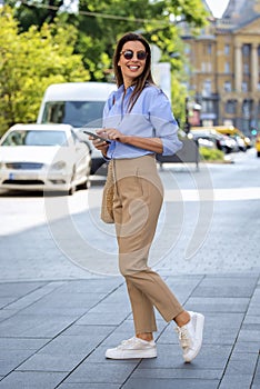 Full length shot of an attractive brunette haired woman walking on the street and using mobile phone