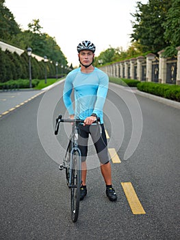 Full length shot of attractive young male cyclist wearing sportswear and protective helmet looking at camera, standing