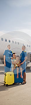 Full length shot of beautiful stewardesses standing near two kids sitting on their luggage in front of big airplane and