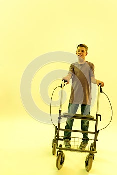 Full length shot of cheerful teenaged disabled boy with cerebral palsy looking at camera, taking steps with his walker