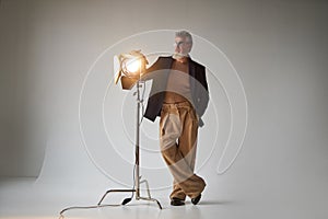 Full length shot of classy middle aged man in glasses looking aside, standing next to studio spotlight while posing for