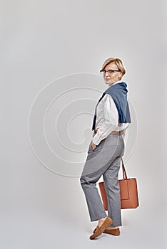 Full length shot of elegant middle aged caucasian woman wearing business attire and glasses looking at camera while