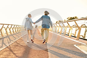 Full length shot of happy lesbian couple holding hands, walking on the bridge and watching the sunrise together