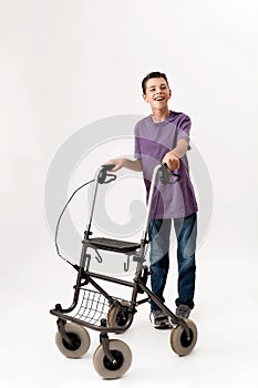 Full length shot of happy teenaged disabled boy with cerebral palsy smiling at camera, taking steps with his walker