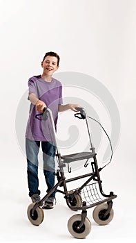 Full length shot of happy teenaged disabled boy with cerebral palsy smiling at camera, taking steps with his walker