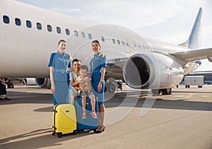 Full length shot of happy two kids sitting on their luggage in front of big airplane on a daytime and smiling at camera