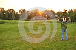 Full length shot of little girl sitting on her father`s shoulders while they enjoying sunset together, daughter and