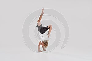 Full length shot of little playful boy child standing on his arms isolated over grey background