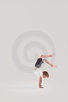 Full length shot of little playful boy child standing on his arms with legs in the air isolated over grey background