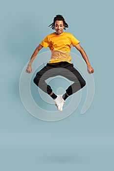 Full length shot of overjoyed black man in orange t-shirt jumping and looking up