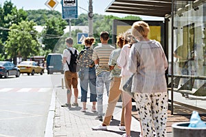Full length shot of people wearing masks waiting, standing in line, keeping social distance at bus stop. Coronavirus