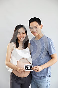 Full length shot of portrait of asian young pregnant belly wife and asian husband holding ultrasound film with happiness and smile