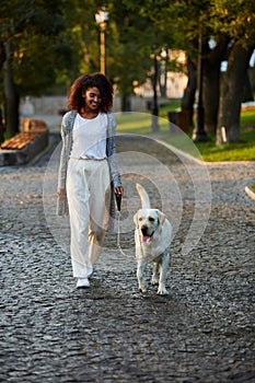 Full-length shot of pretty healthy young lady walking in the morning in park with dog