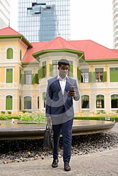 Full length shot of shocked and surprised African businessman outdoors wearing suit and texting with mobile phone