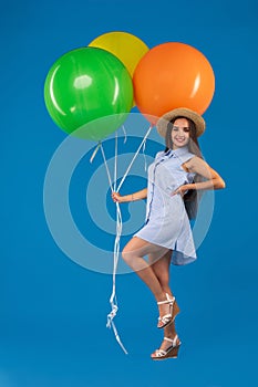 Full-length shot of smiling young woman looking camera and holding colorful air balloons isolated over blue