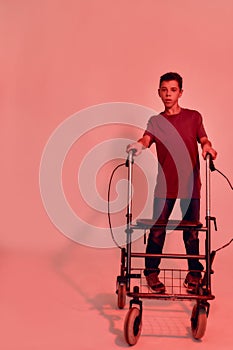 Full length shot of teenaged disabled boy with cerebral palsy looking at camera, taking steps with his walker isolated