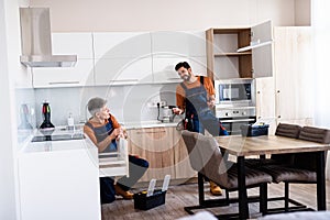 Full length shot of two handymen, workers in uniform talking while assembling kitchen cabinet using screwdriver indoors