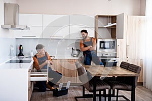 Full length shot of two handymen, workers in uniform talking while assembling kitchen cabinet using screwdriver indoors