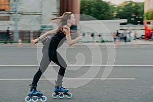 Full length shot of young slim woman rollerblades along asphalt on street enjoys speed spends free time on favorite