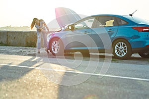 Full length shot of young woman trying to repair her broken car with open hood on her own while waiting for assistance