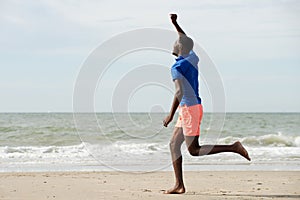 Full length side of happy young man running at beach with arms raised