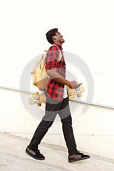 Full length side of handsome young african american male student with skateboard and bag walking outdoors