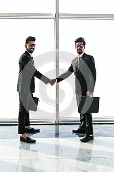 Full length side view of asian businessmen shaking hands in office building with panoramic glasses