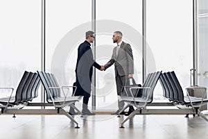 Full length side view of businessmen shaking hands in airport terminal