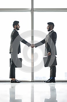 Full length side view of businessmen shaking hands in office building