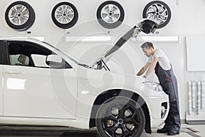 Full length side view of male mechanic examining car engine in repair shop