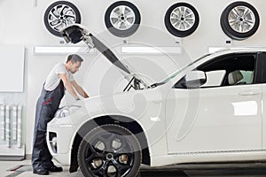 Full length side view of male mechanic examining car engine in repair shop