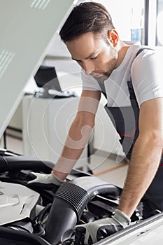 Full length side view of male mechanic examining car engine in repair shop