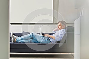 Full-length side view of Middle-aged man using laptop while lying on sofa