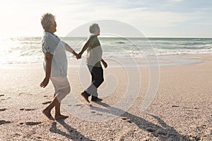 Full length side view of multiracial senior couple holding hands while walking on shore at beach