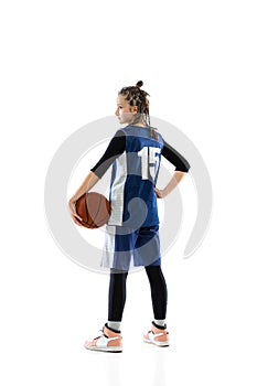 Full-length side view studio shot of young girl, basketball player in blue uniform posing isolated over white background