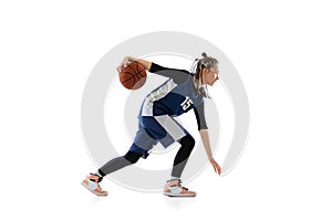 Full-length side view studio shot of young girl, basketball player in blue uniform training isolated over white