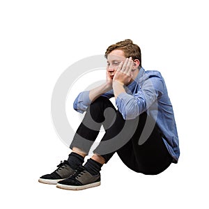 Full length side view of upset and tired boy teenager sitting on the floor keeps hands under chin looking down thoughtful isolated