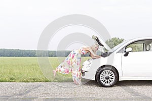 Full-length side view of woman examining broken down car on country road