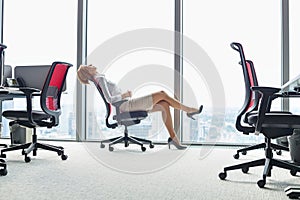 Full length side view of young businesswoman leaning back in chair at office